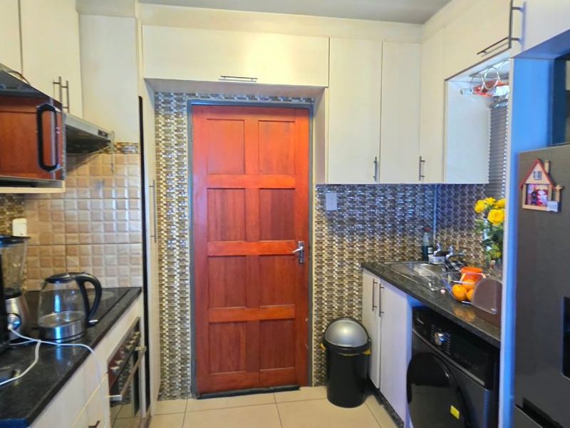 A functional kitchen featuring white cabinetry, tiled backsplash, integrated oven, and a timber door leading to the exterior.