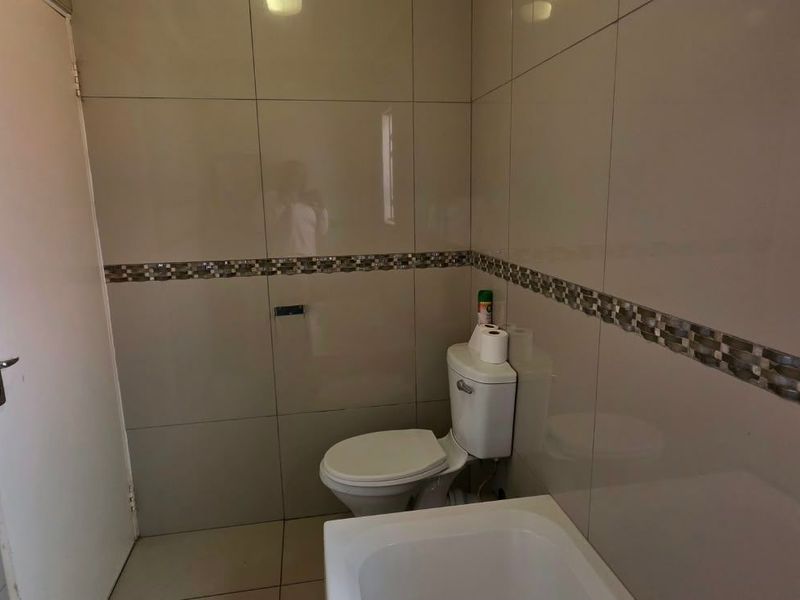 A clean, tiled bathroom featuring a standard toilet, bathtub, and decorative mosaic tile border.