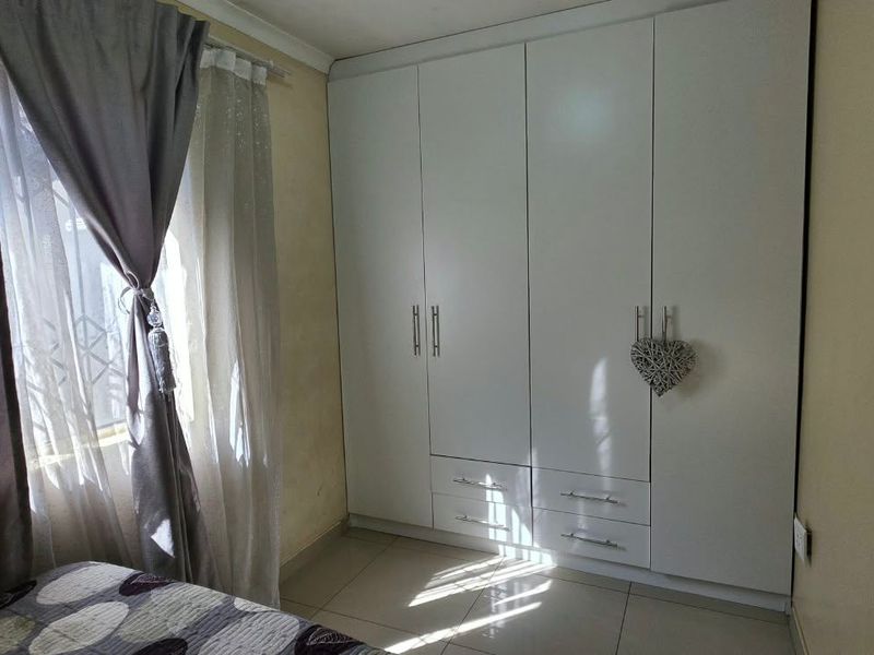 A bedroom featuring tiled flooring and a modern white built-in wardrobe with integrated drawers.