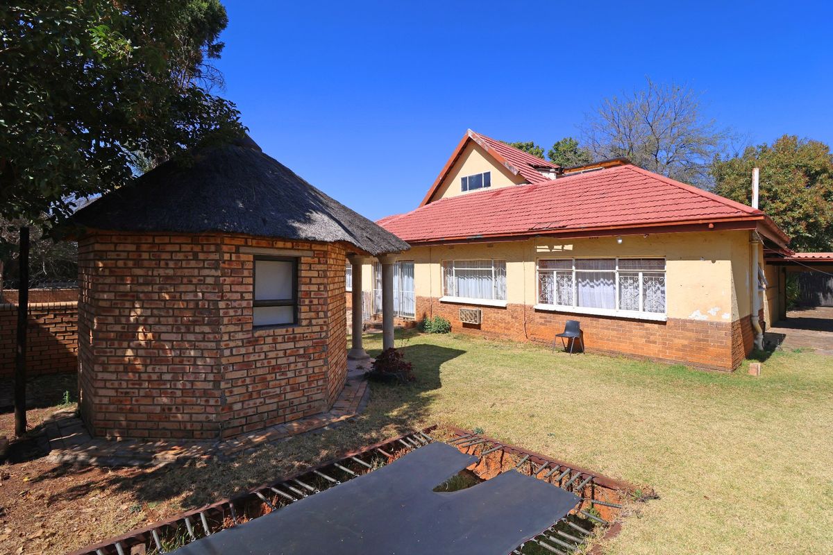 Rear view of the property featuring a brick lapa, tiled roof main house, and a spacious garden area.