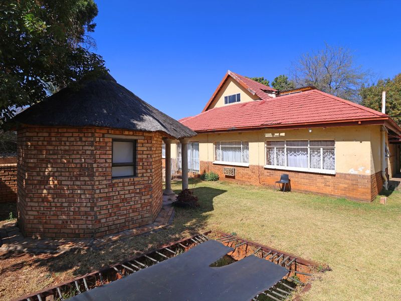 Rear view of the property featuring a brick lapa, tiled roof main house, and a spacious garden area.