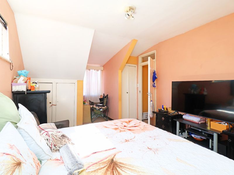 A bedroom featuring sloped ceilings, built-in storage cupboards, and a window, requiring cosmetic updates to improve the overall finish and appeal.