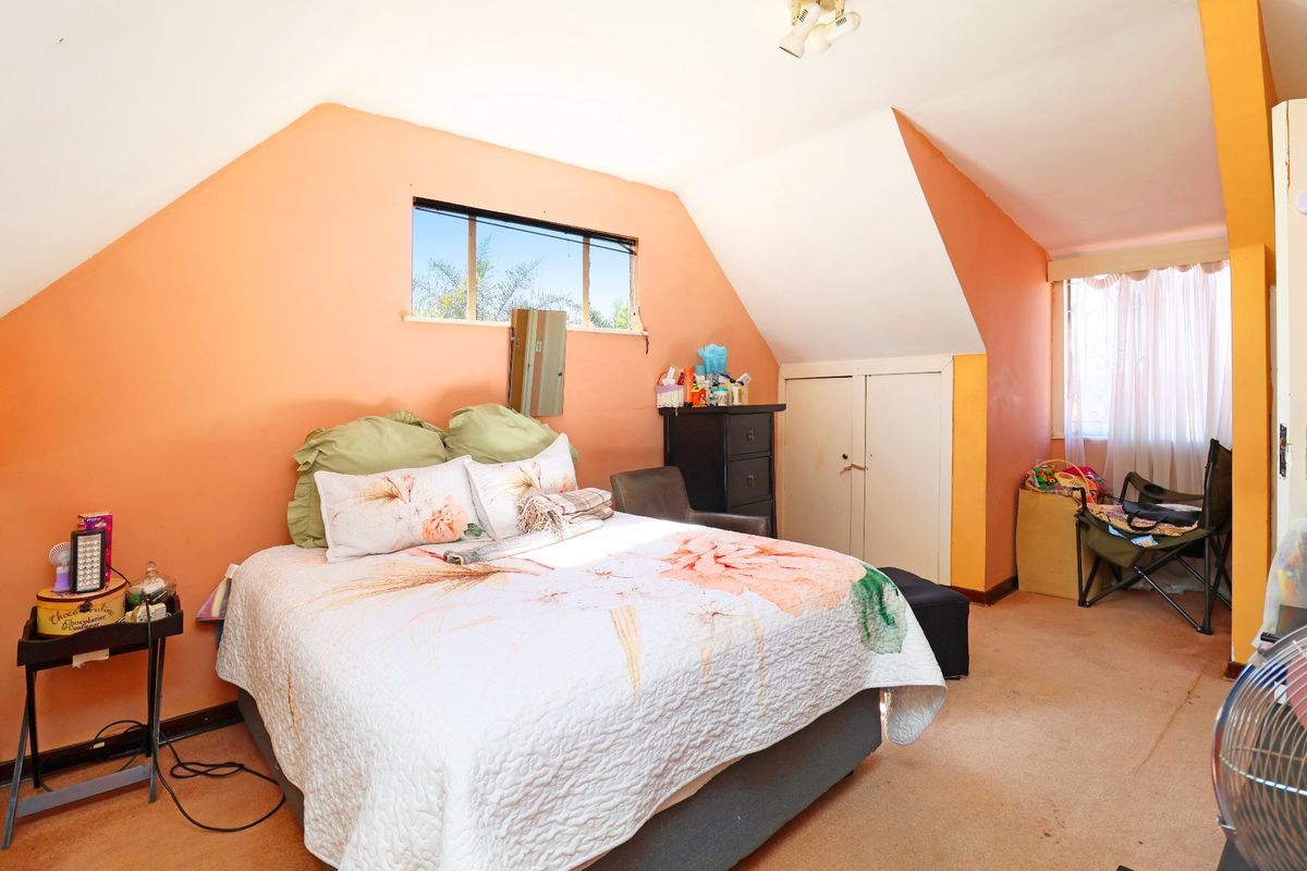 A bedroom featuring sloped ceilings, built-in storage, and natural light from multiple windows, currently requiring cosmetic updates to the flooring and wall finishes.