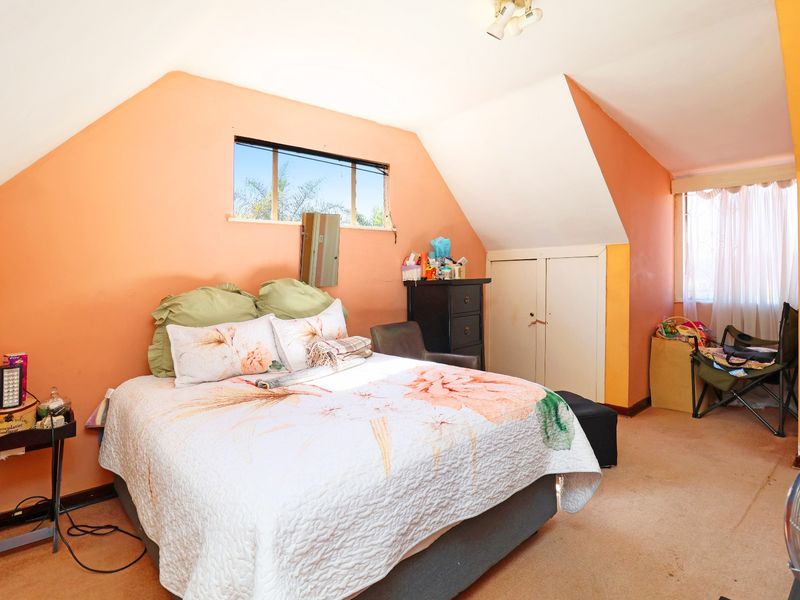 A bedroom featuring sloped ceilings, built-in storage, and natural light from multiple windows, currently requiring cosmetic updates to the flooring and wall finishes.