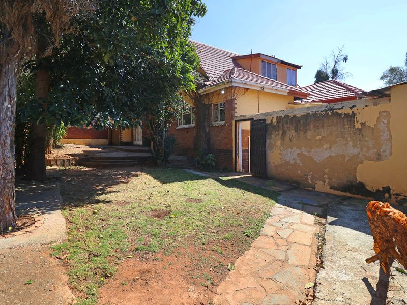 Rear exterior view of the property featuring a garden area, stone pathway, and boundary wall with visible wear to the exterior finishes.