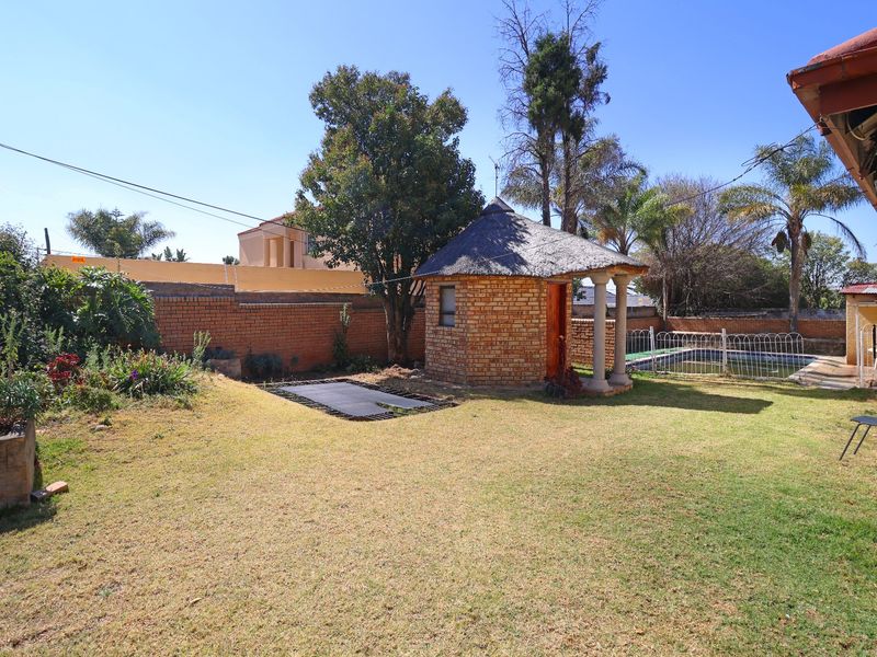 Rear garden featuring a thatched lapa, brick boundary walls, and a swimming pool with metal safety fencing.