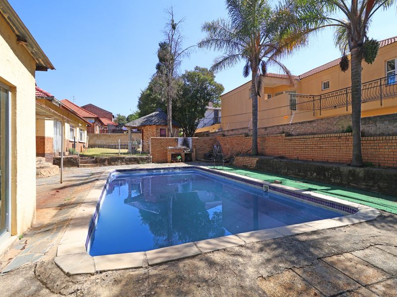Outdoor pool area featuring a swimming pool, built-in braai, and brick boundary walls, set within a paved backyard space.