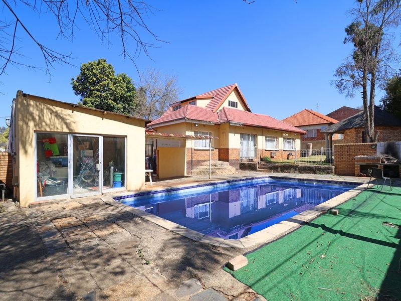 Outdoor pool area featuring a swimming pool, built-in braai, and paved surround, adjacent to the main house and a secondary structure.