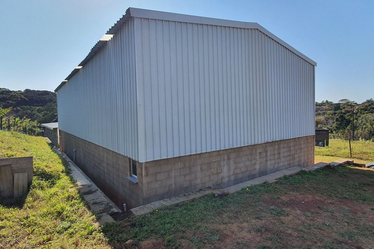 Rear view of an industrial warehouse building featuring corrugated metal upper walls and a concrete block base on a sloped site.