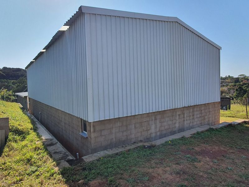 Rear view of an industrial warehouse building featuring corrugated metal upper walls and a concrete block base on a sloped site.