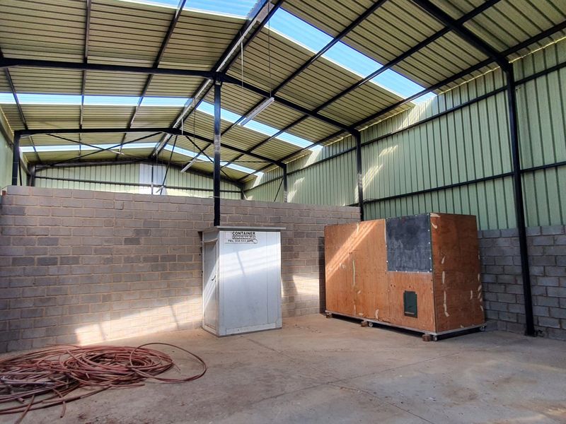 Spacious industrial utility area featuring a high-clearance steel frame structure, corrugated metal roofing with skylights, and durable concrete block walls.