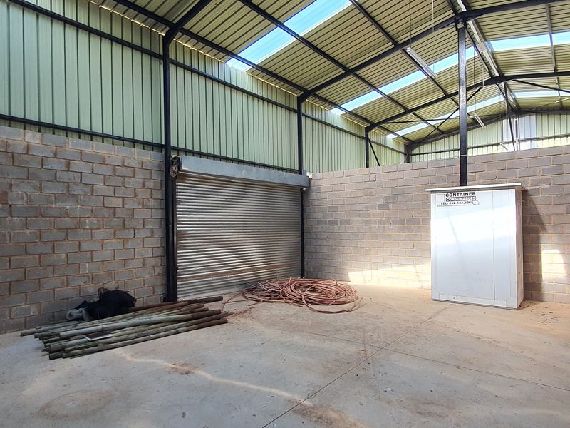 Spacious industrial utility area featuring high ceilings with skylights, concrete flooring, cinder block walls, and a secure roller shutter door.