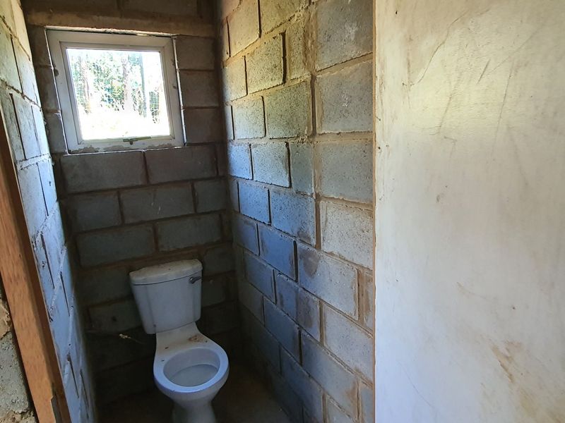 A small, unfinished bathroom featuring exposed concrete block walls and a standard toilet, requiring wall finishes and general renovation to complete.