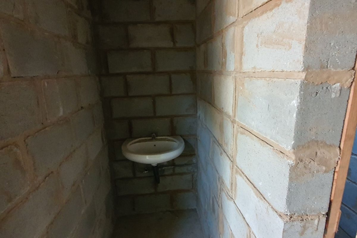 A small, unfinished bathroom space featuring exposed concrete block walls and a simple wall-mounted basin.