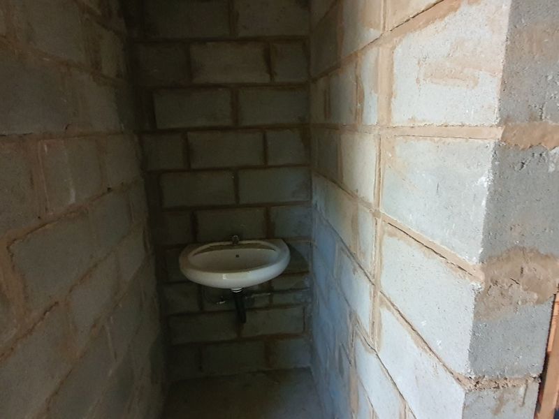 A small, unfinished bathroom space featuring exposed concrete block walls and a simple wall-mounted basin.