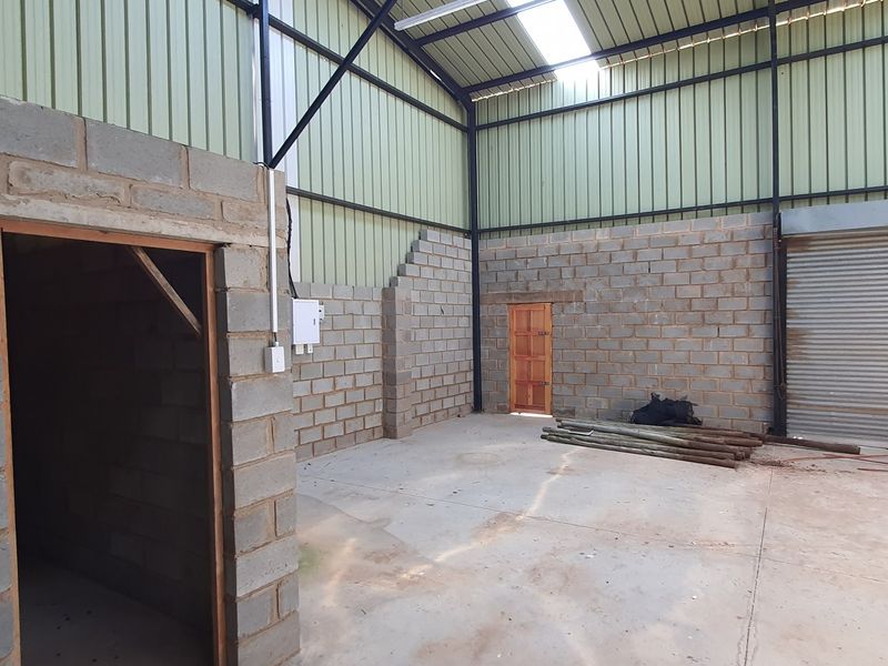 Spacious industrial utility space featuring exposed steel trusses, concrete block walls, a roller shutter door, and natural light from a roof skylight.