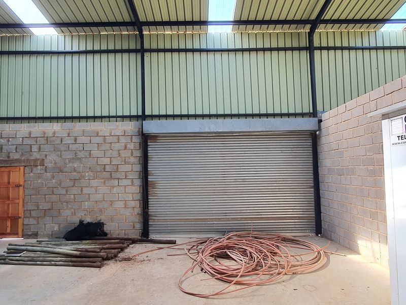 Spacious industrial utility area featuring high ceilings with skylights, concrete block walls, and a large roller shutter door for easy access.