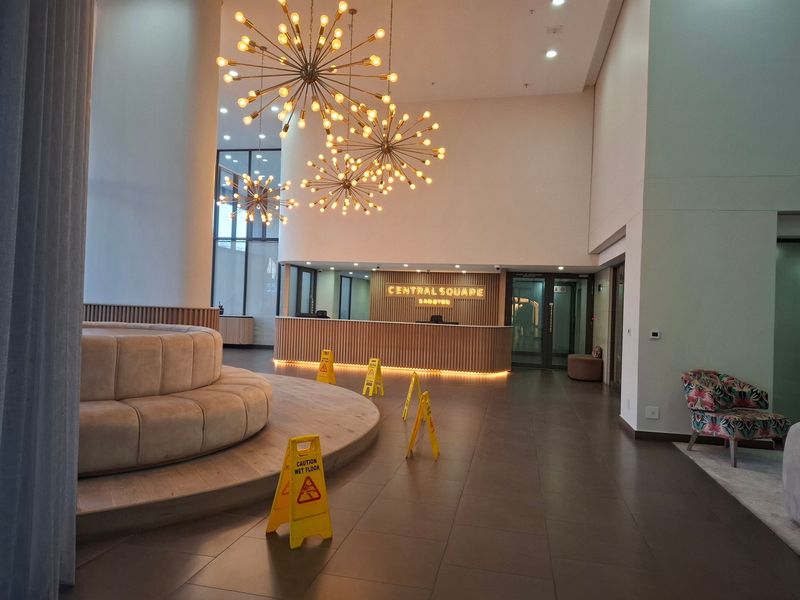 Modern apartment building lobby featuring a reception desk, high ceilings with decorative pendant lighting, and a raised timber seating platform.
