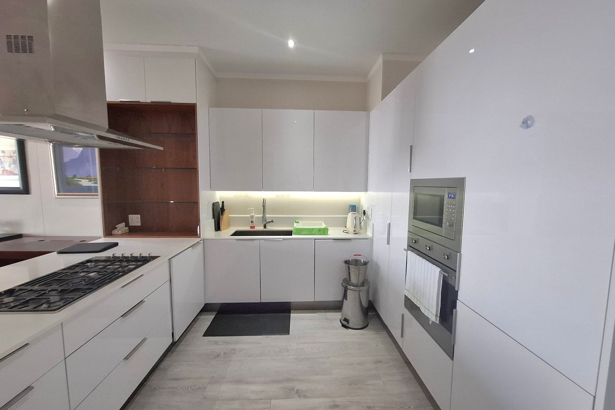 Modern kitchen featuring sleek white cabinetry, integrated appliances including a gas hob and built-in oven, and light-toned laminate flooring.