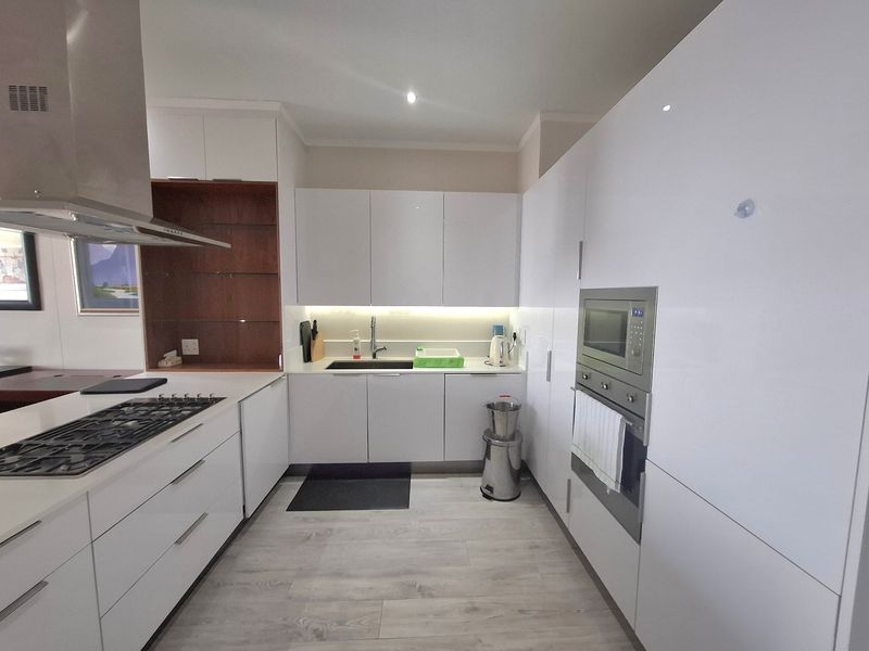 Modern kitchen featuring sleek white cabinetry, integrated appliances including a gas hob and built-in oven, and light-toned laminate flooring.