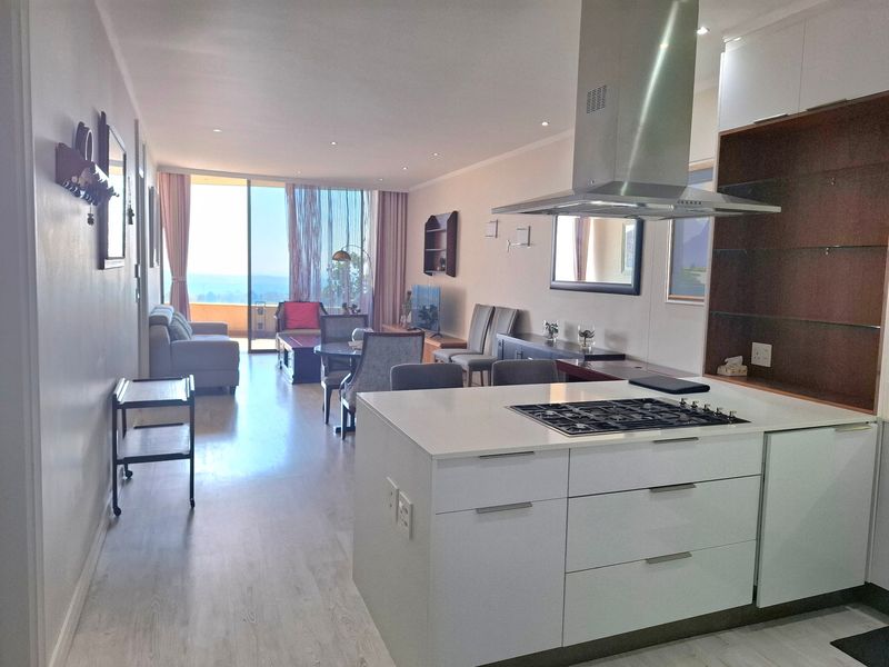 Modern open-plan living area featuring a sleek kitchen with a central island, gas hob, and seamless flow to a balcony with scenic views.