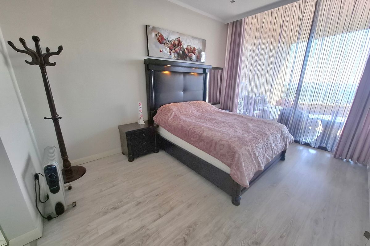 A well-lit bedroom featuring light-toned laminate flooring, recessed ceiling lighting, and large sliding glass doors providing access to an adjoining balcony.