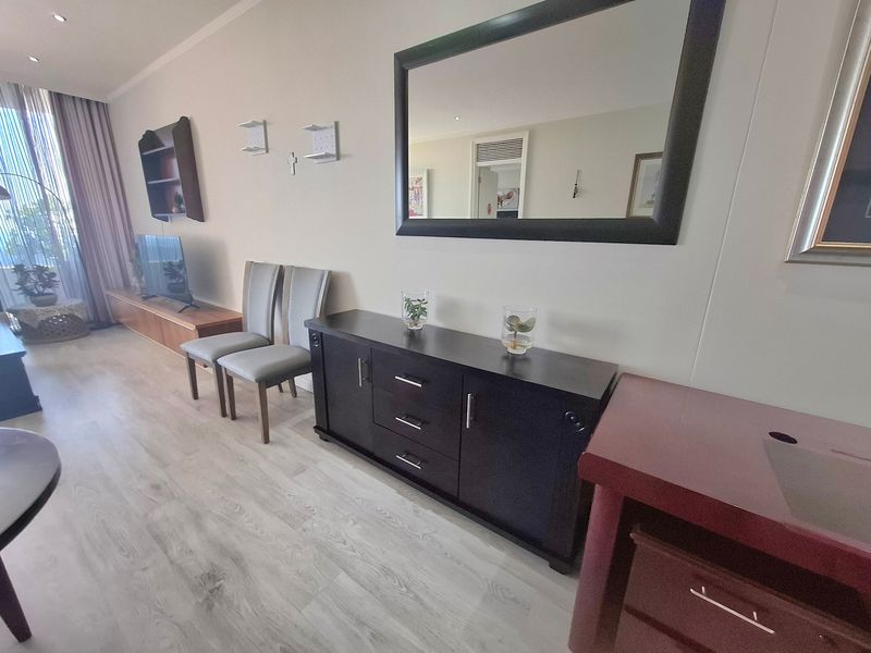 A well-maintained living room featuring light-toned laminate flooring, recessed ceiling lighting, and access to a balcony through a sliding glass door.