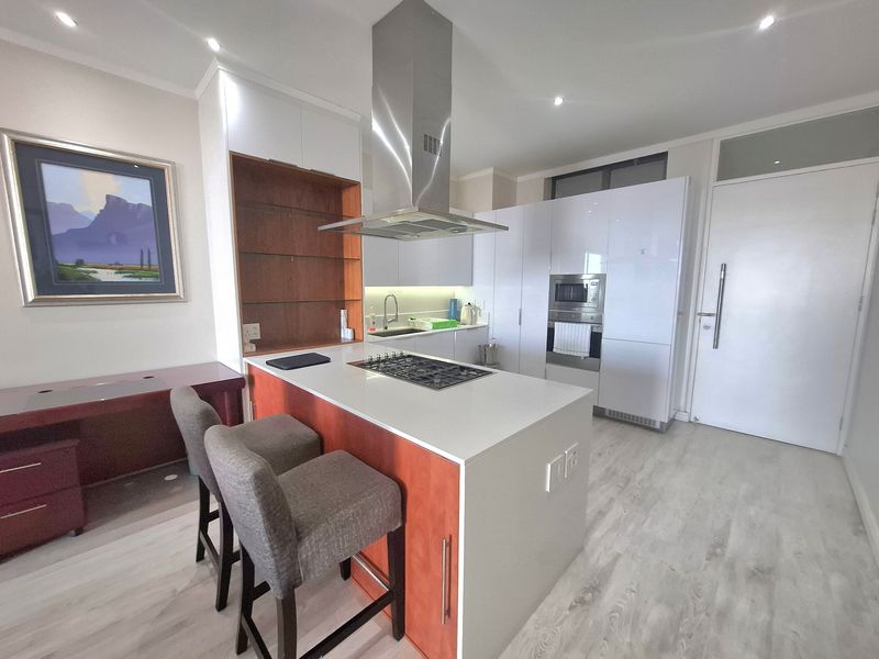 Modern kitchen featuring a central island with a gas hob, stainless steel extractor, built-in oven, microwave, and sleek cabinetry with integrated appliances.