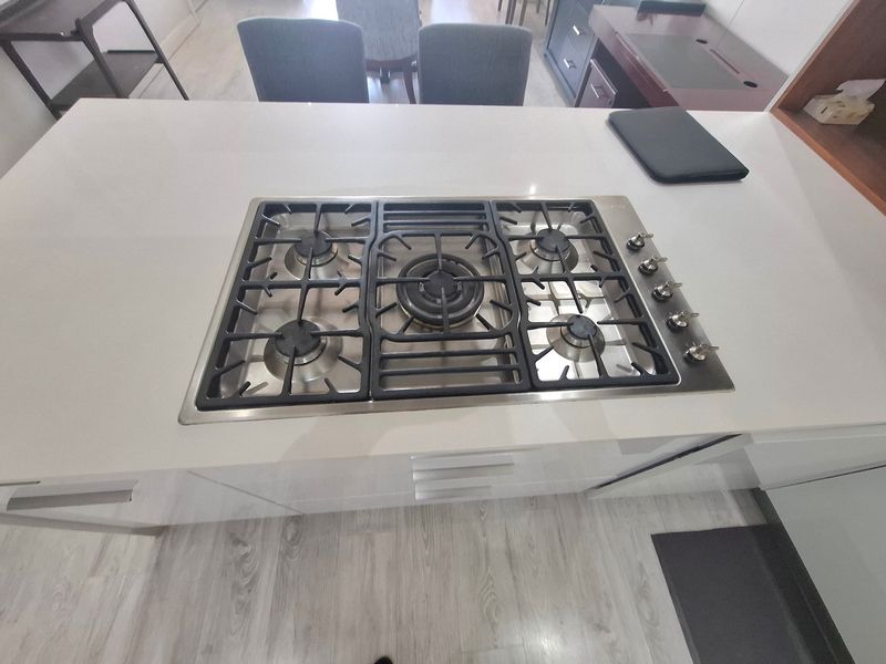 A modern kitchen island featuring a built-in five-burner gas cooktop set into a clean stone countertop with integrated cabinetry below.