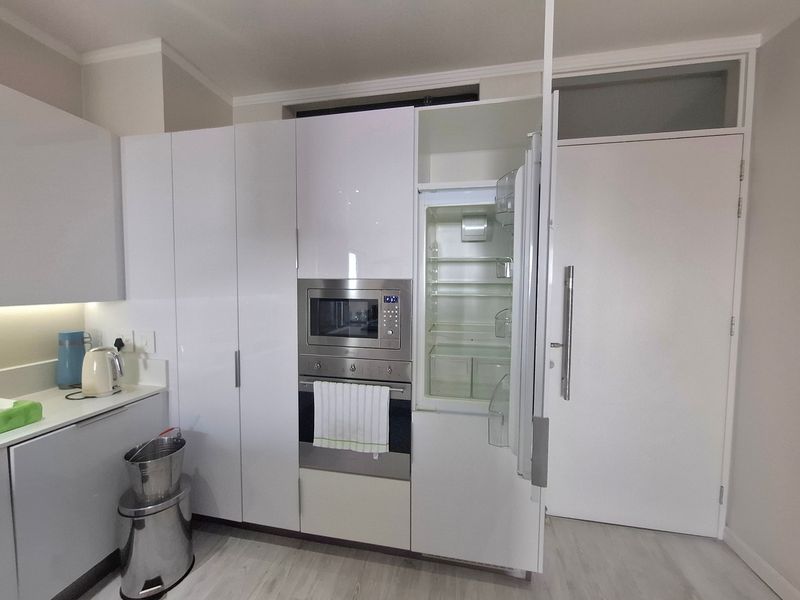 Modern kitchen featuring sleek white gloss cabinetry, integrated appliances including an oven and microwave, and a clean stone countertop with under-cabinet lighting.
