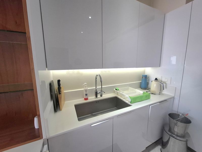 Modern kitchen area featuring sleek glossy cabinetry, a stone countertop, an undermount sink with a gooseneck faucet, and integrated under-cabinet lighting.