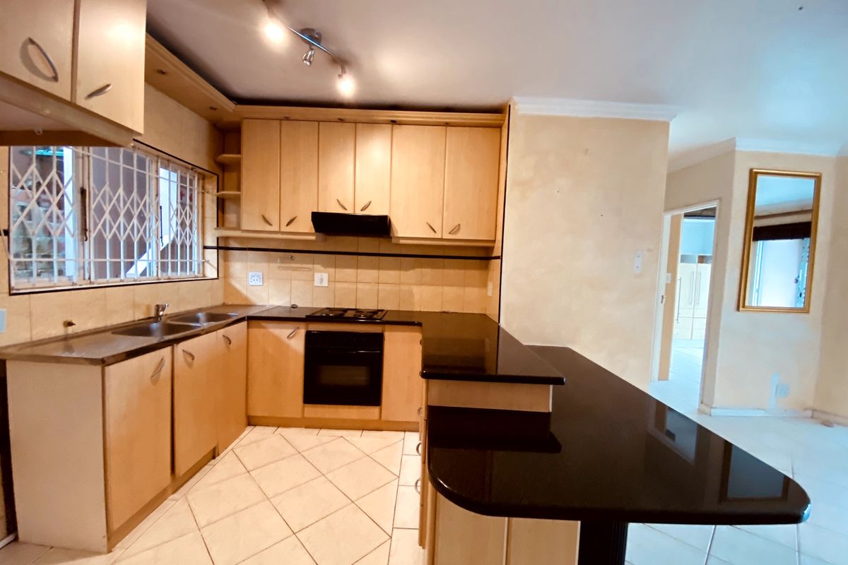 A functional kitchen featuring light wood cabinetry, black granite countertops, built-in oven and hob, and tiled flooring with a breakfast bar extension.