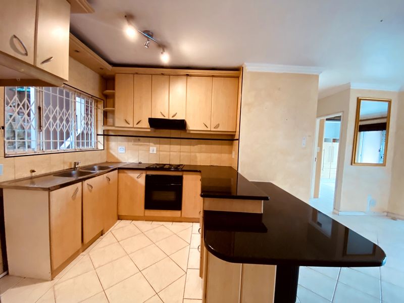 A functional kitchen featuring light wood cabinetry, black granite countertops, built-in oven and hob, and tiled flooring with a breakfast bar extension.