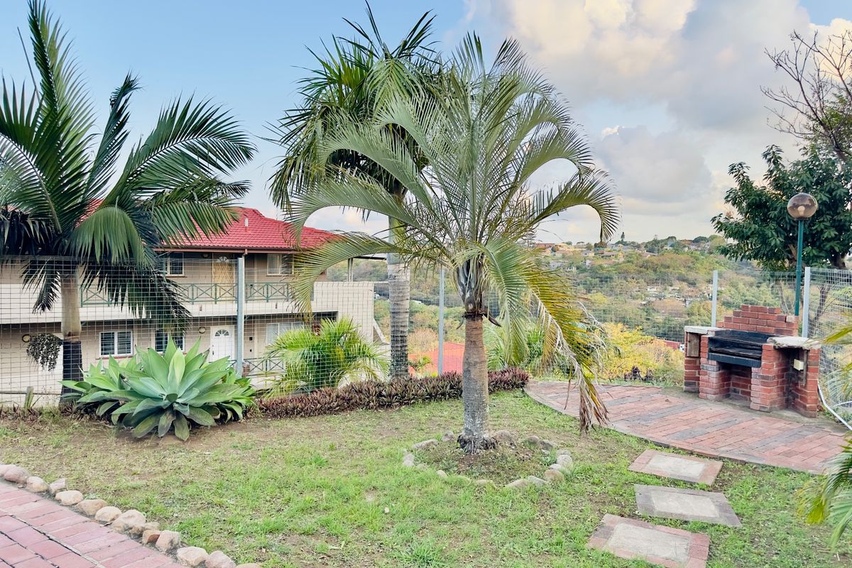 Rear garden area featuring a brick built-in braai, paved pathways, and established landscaping with views of the surrounding neighborhood.