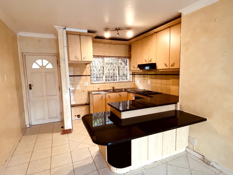 A functional kitchen featuring light wood cabinetry, black granite countertops, a built-in hob with extractor, and tiled flooring.