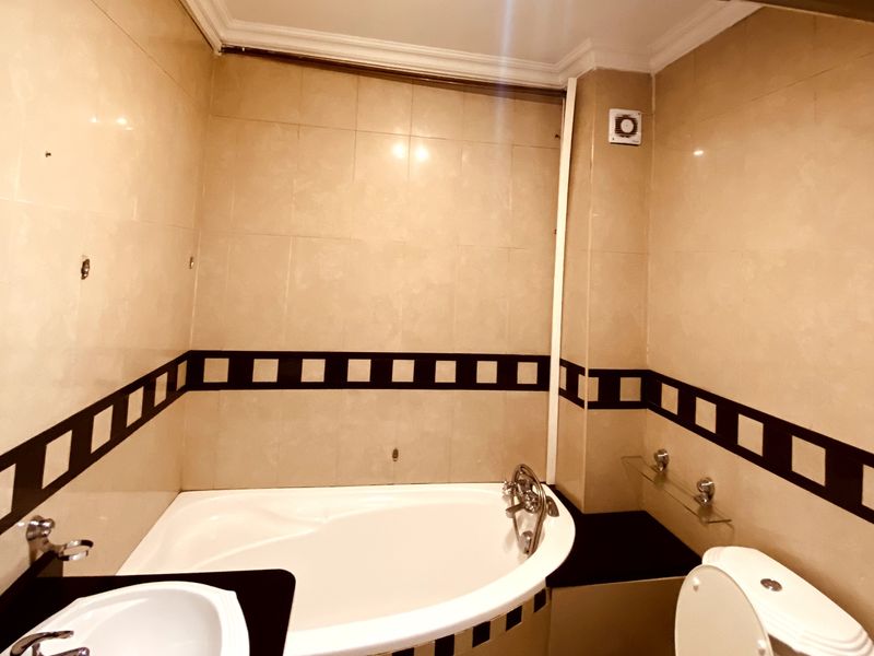 A compact bathroom featuring a built-in bathtub, vanity basin, and toilet with neutral wall tiling and a decorative border.