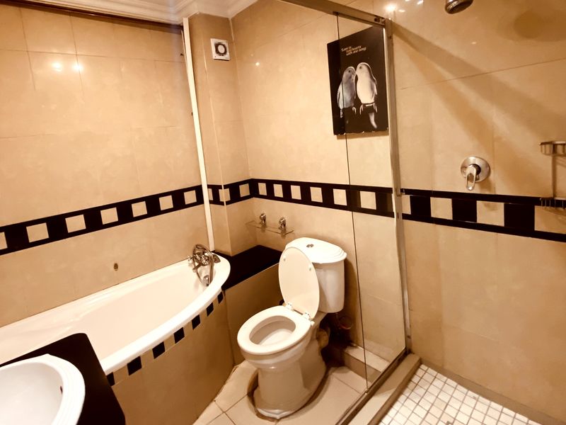 A functional bathroom featuring a bathtub, separate shower enclosure with glass screen, toilet, and vanity sink with tiled finishes.