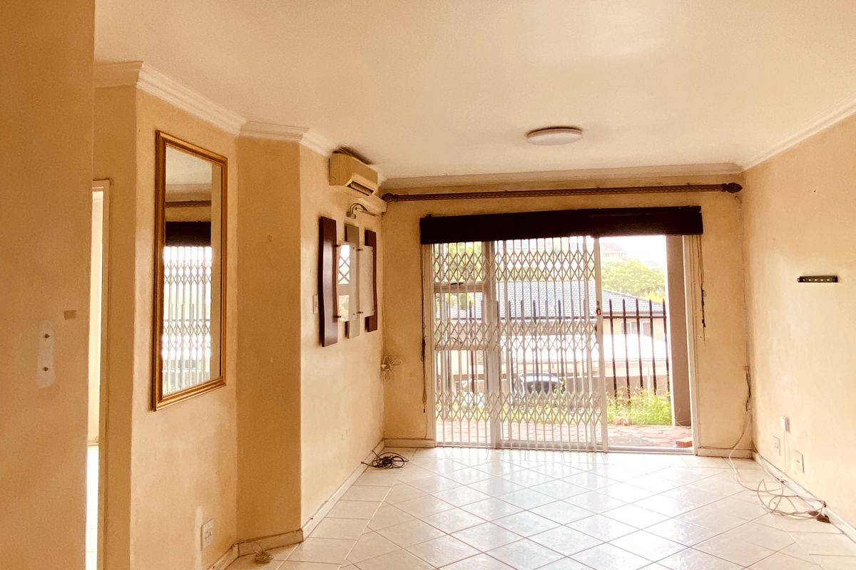 An empty living room featuring tiled flooring, crown molding, and a sliding glass door with a security gate leading to an outdoor area.