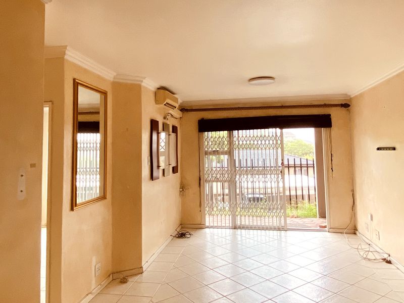 An empty living room featuring tiled flooring, crown molding, and a sliding glass door with a security gate leading to an outdoor area.