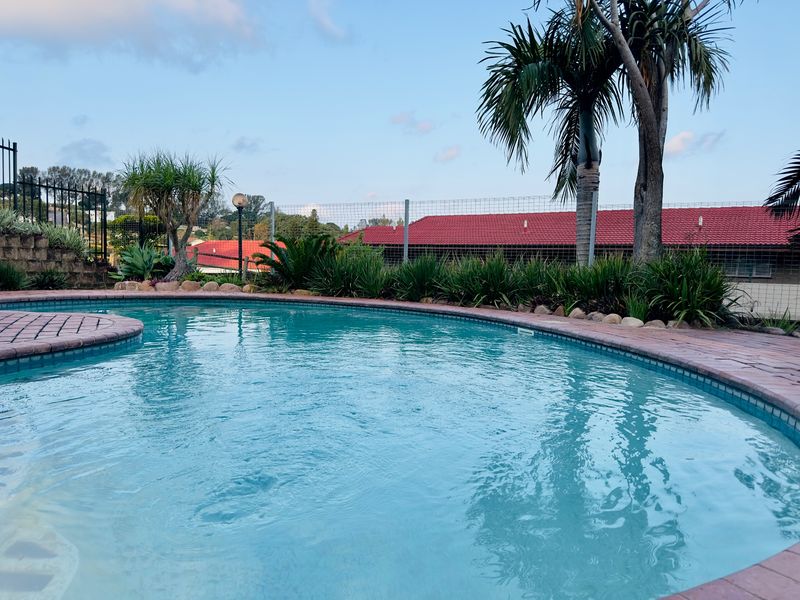 A well-maintained swimming pool area featuring brick coping, established garden landscaping, and secure perimeter fencing.