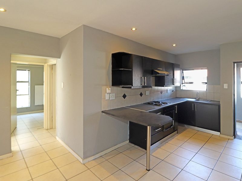 A functional kitchen featuring dark cabinetry, laminate countertops, built-in oven and hob, and tiled flooring, offering a clean and practical workspace.