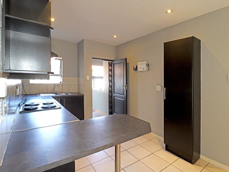 A functional kitchen featuring dark cabinetry, laminate countertops, an electric hob, and tiled flooring, offering a clean and practical workspace.