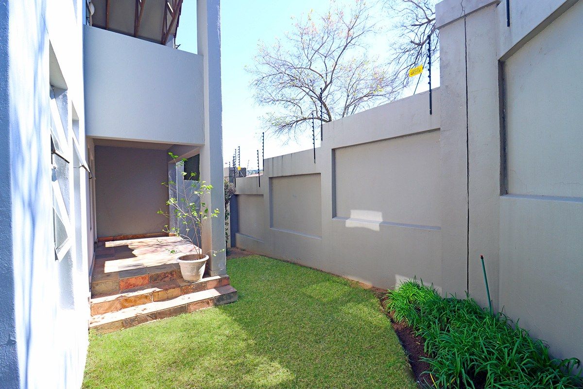 A private rear garden area featuring a tiled patio, well-maintained lawn, and high perimeter walls equipped with electric fencing for added security.