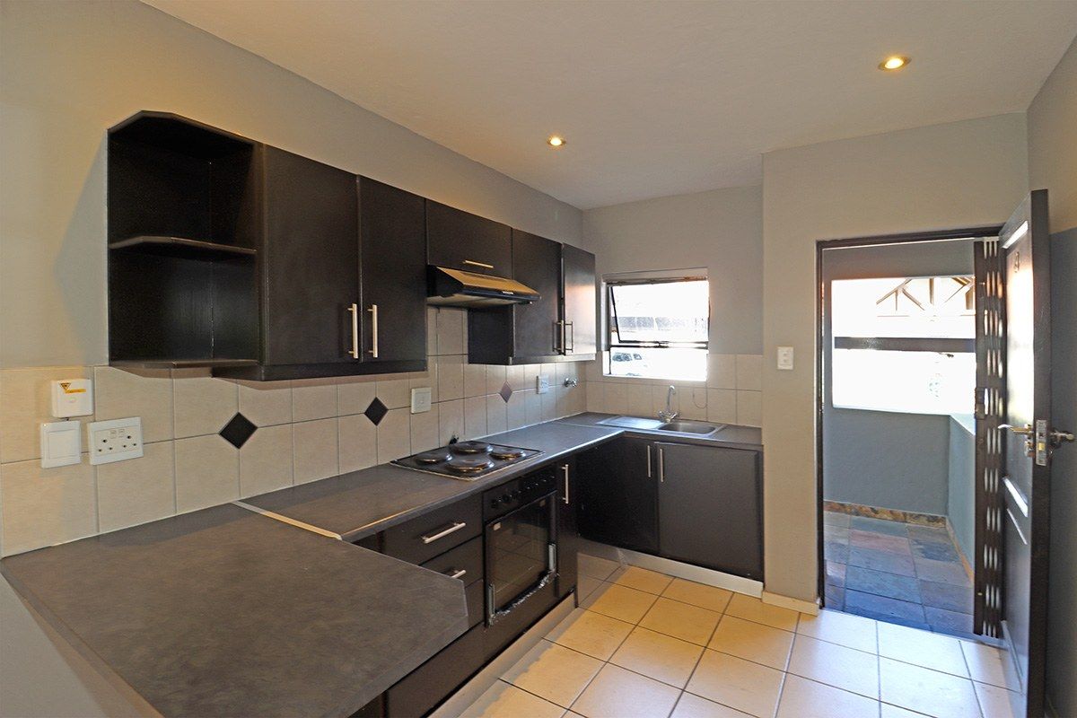 A functional kitchen featuring dark cabinetry, built-in oven and hob, tiled backsplash, and direct access to an outdoor area.