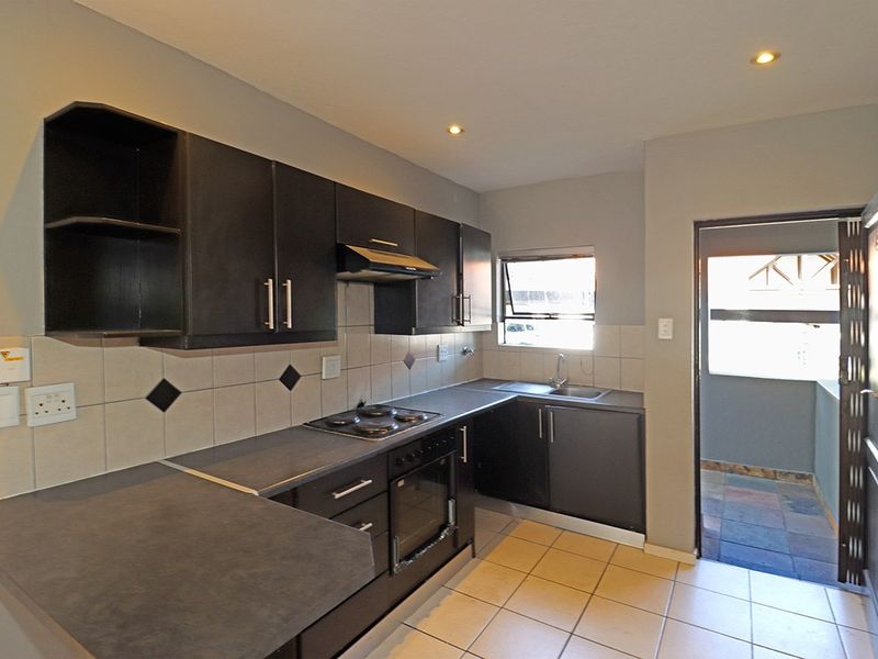 A functional kitchen featuring dark cabinetry, built-in oven and hob, tiled backsplash, and direct access to an outdoor area.