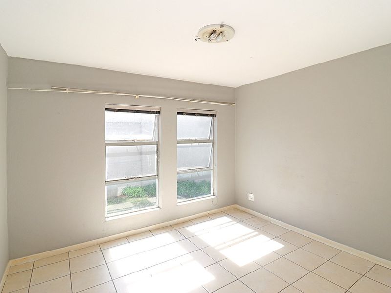 A vacant bedroom featuring neutral grey walls, tiled flooring, and dual windows with aluminium frames, offering a blank canvas for personalization.
