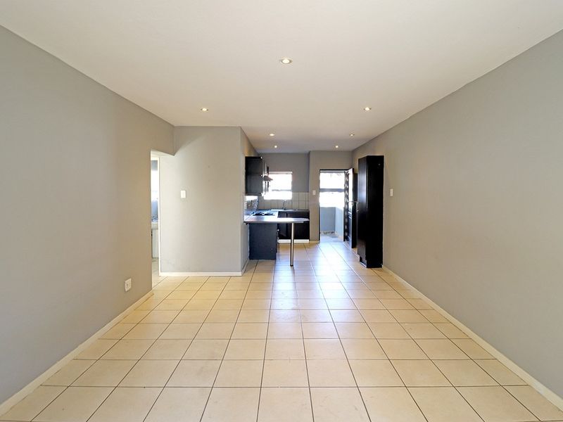 An open-plan living and kitchen area featuring neutral grey walls, tiled flooring, and recessed lighting, providing a clean and versatile space.