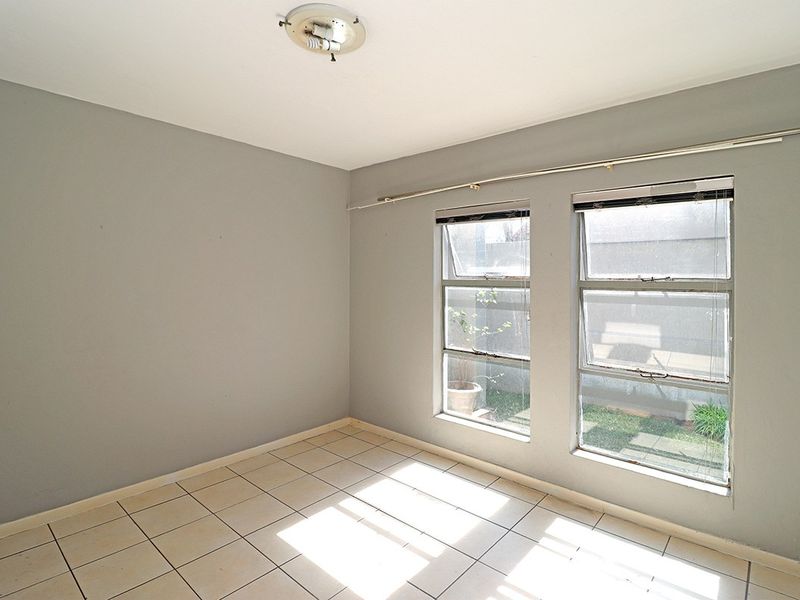 An empty bedroom featuring tiled flooring, grey painted walls, and aluminium-framed windows with curtain tracks.