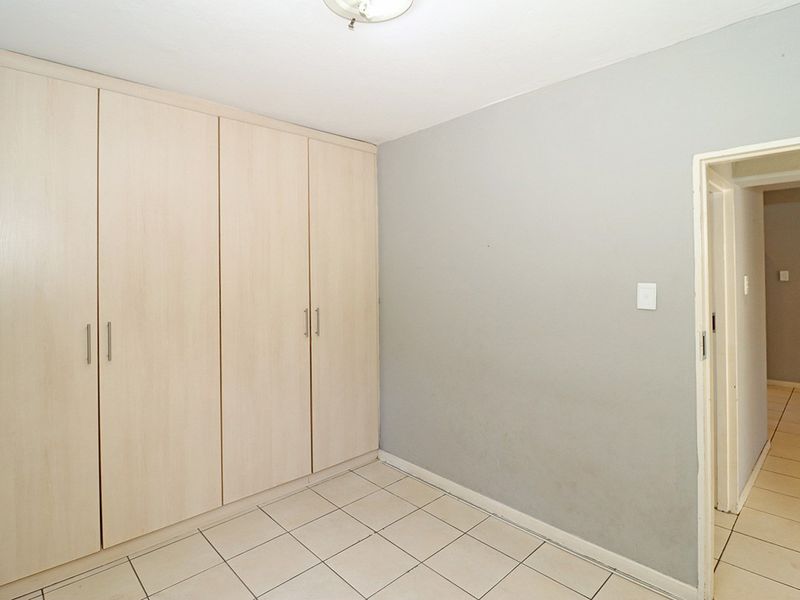 A clean, empty bedroom featuring light-toned built-in cupboards, neutral tiled flooring, and a simple ceiling light fixture.