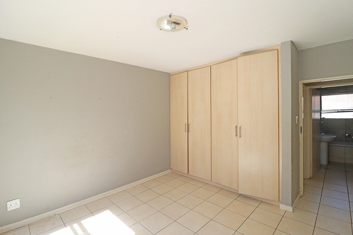 An empty bedroom featuring neutral tiled flooring, built-in wooden cupboards, and a view into the adjacent bathroom.